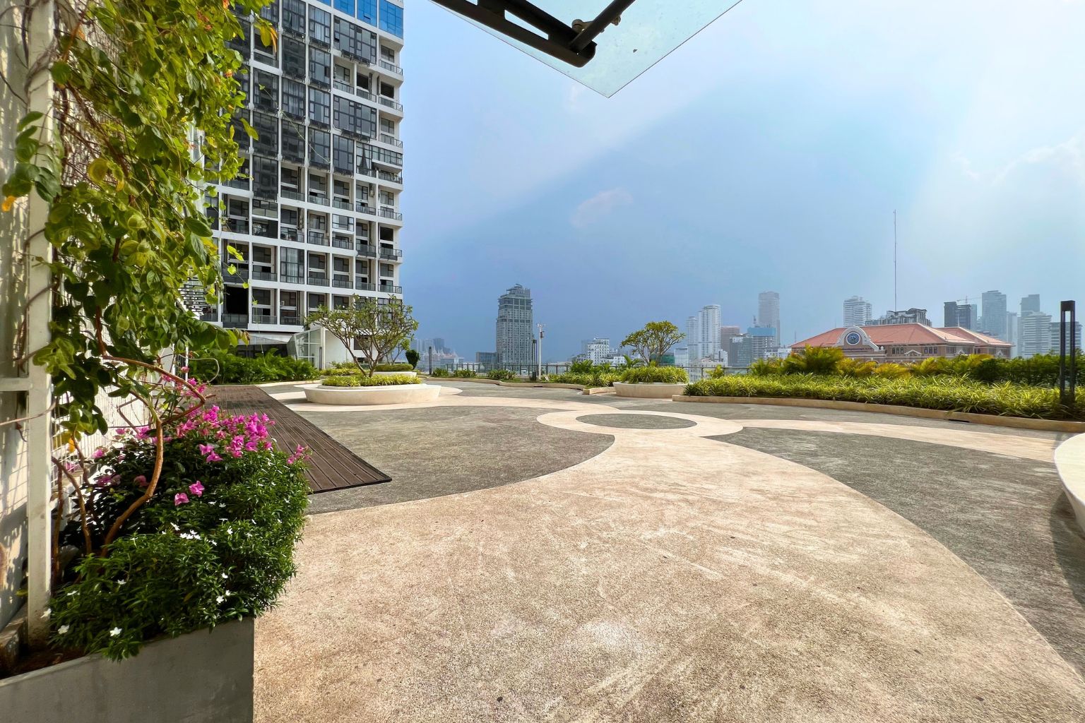 Un jardin sur le toit offrant une vue sur les gratte-ciel d’une ville, avec un bâtiment moderne doté de balcons et un ciel dégagé.