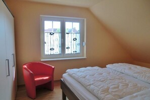 A bedroom with a bed, a red chair, and a window with a view of a fence and trees. - Holiday home in Zingst with swimming pool (Zingst)