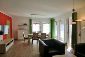 Ein modernes Wohnzimmer mit Flachbildfernseher, einer Essecke mit Tisch und Stühlen sowie einer Küchenzeile mit Schränken und Arbeitsplatte.