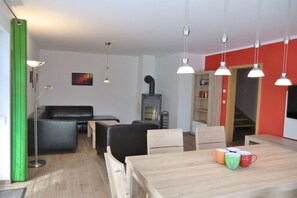 Ein modernes Wohnzimmer mit einer Couch, einem Esstisch mit bunten Tassen, einem Kamin und Pendelleuchten.