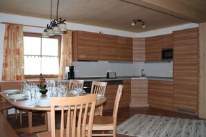 A modern kitchen with wooden cabinets, a dining table set for four, and a large window with curtains. - Holiday home in Going with swimming pool (Going)