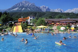A swimming pool with people, a water slide, and mountains in the background. - Holiday home in Going with swimming pool (Going)