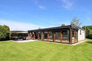 A modern house with a glass conservatory, a patio with outdoor furniture, and a well-maintained lawn. - Holiday home with 4 bedrooms (Scharbeutz)