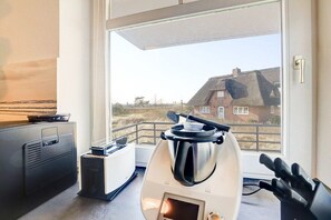 A kitchen with a modern stove, a toaster, and a window with a view of a house. - Holiday apartment with 2 bedrooms (Sankt Peter-Ording)
