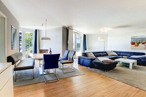 A modern living room with a sofa, chairs, a coffee table, and a dining area with a bench and table. - Holiday apartment with 2 bedrooms (Sankt Peter-Ording)
