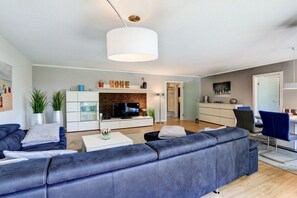 A modern living room with a sofa, TV, and a dining area with chairs. - Holiday apartment with 2 bedrooms (Sankt Peter-Ording)