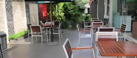 Un patio al aire libre con mesas y sillas, rodeado de follaje y un edificio de diseño moderno.