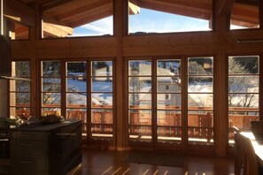 Tilava huone, jossa on suuret ikkunat, puiset kattopalkit ja näkymä lumiseen maisemaan.