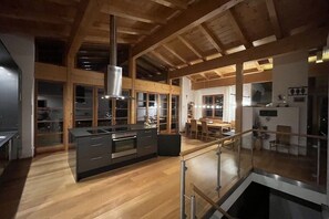 A modern kitchen with a central island, wooden beams, and a glass railing overlooking a dining area. - Cabin with 1 bedroom (Maria Alm - Hinterthal)