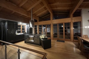 A modern kitchen with a central island, wooden beams, and large sliding glass doors. - Cabin with 1 bedroom (Maria Alm - Hinterthal)