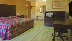 Een hotelkamer met een bed, bureau, stoel, plafondventilator en een in de achtergrond zichtbare badkamer.