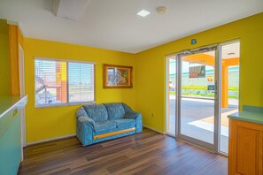 A room with a blue sofa, yellow walls, a window with blinds, and a door leading outside. - Executive Inn And Suites (San Benito)