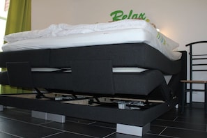 Una cama con colchón y cabecera, una mesita de noche y una pared con un cartel verde.