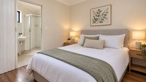 A bedroom with a bed, bedside tables, a nightstand, a framed plant, and a bathroom visible through an open door. - Great location 3 bed 2 bath property -Available for Short term rental Only (Kenwick)