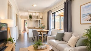 A modern living room with a sofa, coffee table, and TV. There is a kitchen area in the background with a dining table and chairs. - Great location 3 bed 2 bath property -Available for Short term rental Only (Kenwick)