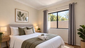 A bedroom with a bed, bedside tables, a window with curtains, a plant, and a framed picture on the wall. - Great location 3 bed 2 bath property -Available for Short term rental Only (Kenwick)
