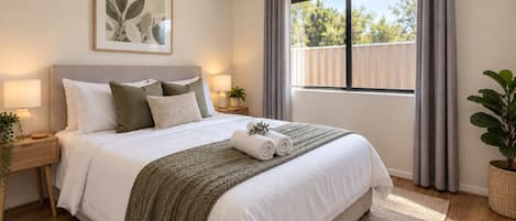 A bedroom with a bed, bedside tables, a window with curtains, a plant, and a framed picture on the wall.