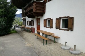 Ein Gebäude mit Holzbanken und Tischen vor der Fassade, einer Tür und Fenstern mit Holzläden.