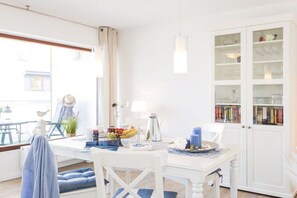 A bright dining area with a white table, chairs, and a glass cabinet with books. - Holiday apartment with 2 bedrooms (Scharbeutz)
