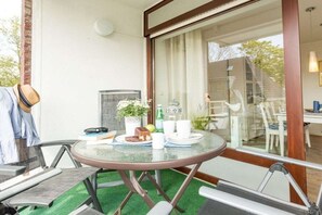 A round glass table with a brown frame, a potted plant, a cake, and white cups and saucers. - Holiday apartment with 2 bedrooms (Scharbeutz)
