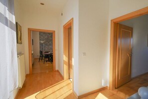 Un couloir avec un plancher en bois, un radiateur et une porte donnant sur une pièce.
