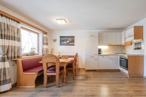 A cozy kitchen with wooden cabinets, a dining table with benches, and a window with curtains. - Country house - Praxmarer (Neustift im Stubaital)