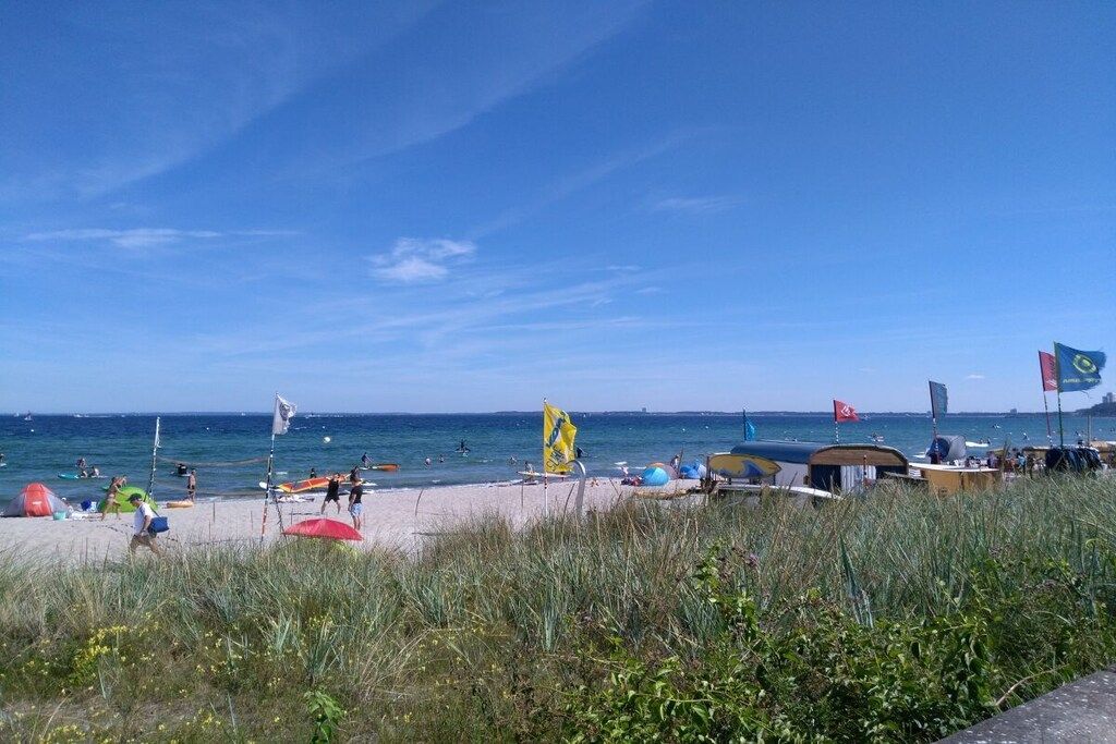Une plage avec des tentes et des drapeaux, un ciel dégagé et une mer calme.