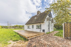 Ein weißes Haus mit geneigtem Dach, einer Holzterrasse und einer gepflasterten Auffahrt zu einem verschlossenen Eingang.