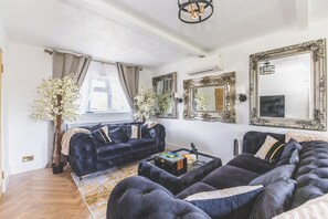 Ein Wohnzimmer mit einer dunkelgrauen Sofagarnitur, einem Couchtisch mit Büchern und einem großen Spiegel mit aufwendigen Rahmen.