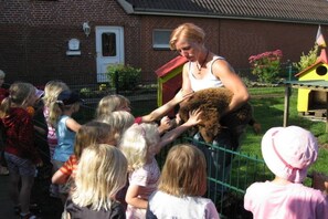 A person interacting with children near a fenced area with a brick building in the background.
