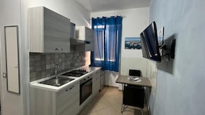 Une cuisine compacte comprenant un évier, une cuisinière et des placards, une petite table à manger et un téléviseur fixé au mur.