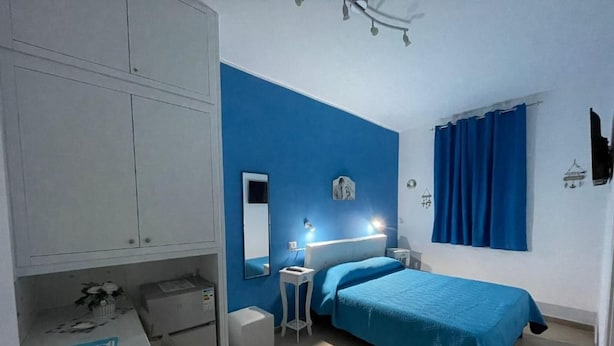 Une chambre à coucher avec un lit, un bureau, une chaise, une armoire et une fenêtre avec des rideaux.