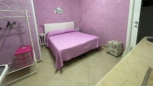 Une pièce comprenant un lit, une petite table de chevet, une étagère fixée au mur et une porte.