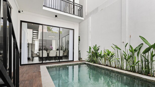 A modern indoor pool area with a wooden deck, a glass-enclosed dining area, and a variety of indoor plants. - Allena Villa by Kozystay - Canggu (Badung)
