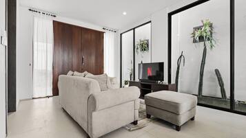 Una sala de estar moderna con un sofá, un reposapiés y un televisor de pantalla plana.
