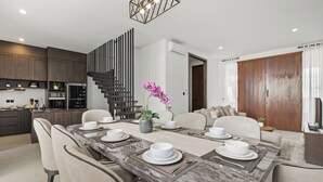 A modern kitchen with dark cabinets, a built-in oven, and a dining area with a marble table set for six. - Allena Villa by Kozystay - Canggu (Badung)