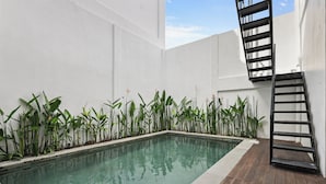 A rectangular swimming pool with clear water, surrounded by a white wall and a wooden deck. - Allena Villa by Kozystay - Canggu (Badung)