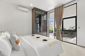 Un dormitorio moderno con cama, puerta corrediza de vidrio hacia un balcón y una ventana con cortinas.