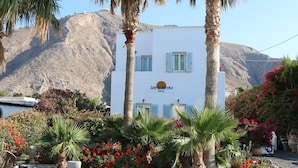 Un hotel llamado 'Spiracos Hiroko' con fachada blanca, palmeras y flores rojas en primer plano.