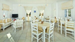 Un comedor con mobiliario blanco, televisor y un amplio ventanal con cortinas.