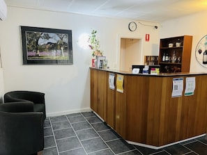 Un área de recepción con un mostrador de madera, un reloj y un cuadro de paisaje en la pared.
