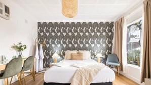 Ein Schlafzimmer mit Bett, Nachttischen, Schreibtisch, Stühlen, einem Fenster mit Vorhängen und einer Wand mit Muster.