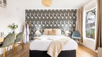 A bedroom with a bed, bedside tables, a desk, chairs, a window with curtains, and a patterned wall.