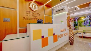 A reception area with a wooden reception desk, a glass counter, and a decorative plant. - Myspace Dhruva Inn (Bengaluru)