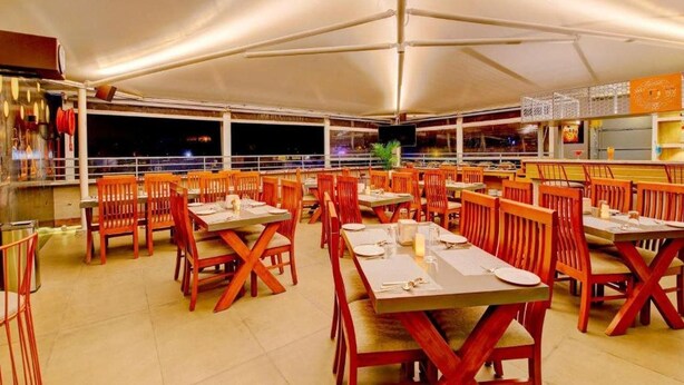 An outdoor dining area with tables and chairs, a covered section, and a view of the night sky. - Myspace Dhruva Inn (Bengaluru)