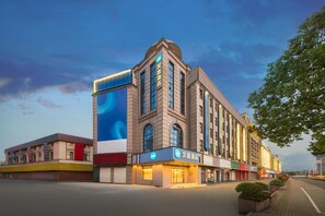 A hotel with a prominent blue advertisement on its facade, multiple windows, and a well-lit entrance. - Hanting Hotel Shanghai Songjiang Siting (Shanghai)