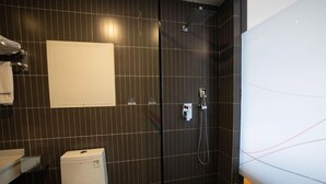 Een moderne badkamer met een donkere betegelde muur, een wit toilet, een douche met een handdouche en een handdoekhouder met een witte handdoek.