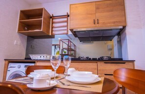 A compact kitchen with wooden cabinets, a built-in washing machine, and a dining area with a table set for two. - Timurbay Seafront Apartment by My Seasons (Kuantan)