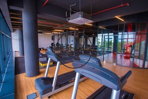 A modern gym with treadmills, weight machines, and a large window offering a view of the outdoors. - Timurbay Seafront Apartment by My Seasons (Kuantan)