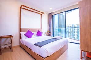 A modern hotel room with a large bed, wooden headboard, and a view of the city through a large window. - Timurbay Seafront Apartment by My Seasons (Kuantan)